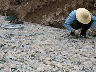 A worker is fastening the lids to the side panels of the gabion mattress.